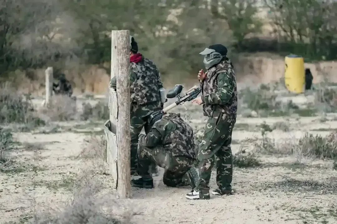 A group of people in camouflage playing paintball or airsoft in the woods